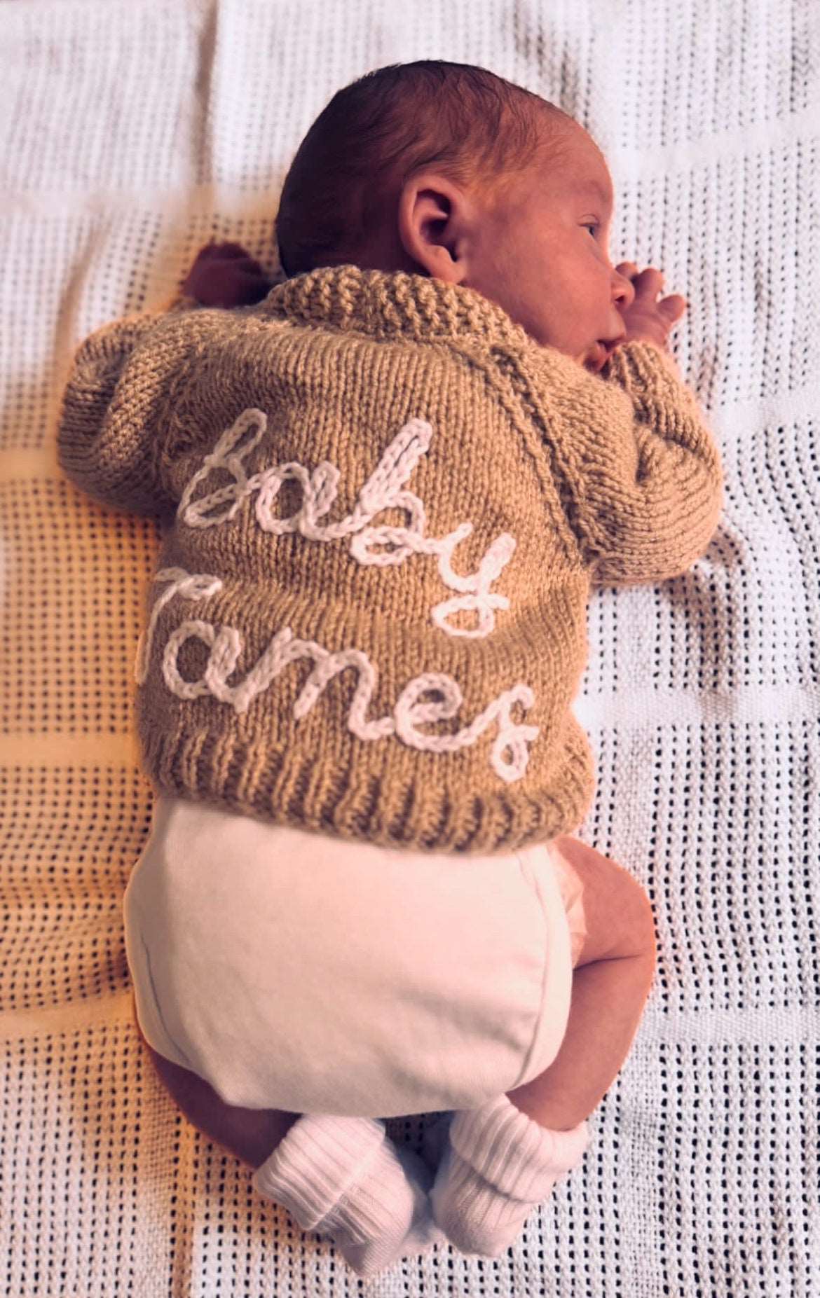 Newborn baby wearing a hand knitted cardigan with 'Baby James' hand embroidered on the back