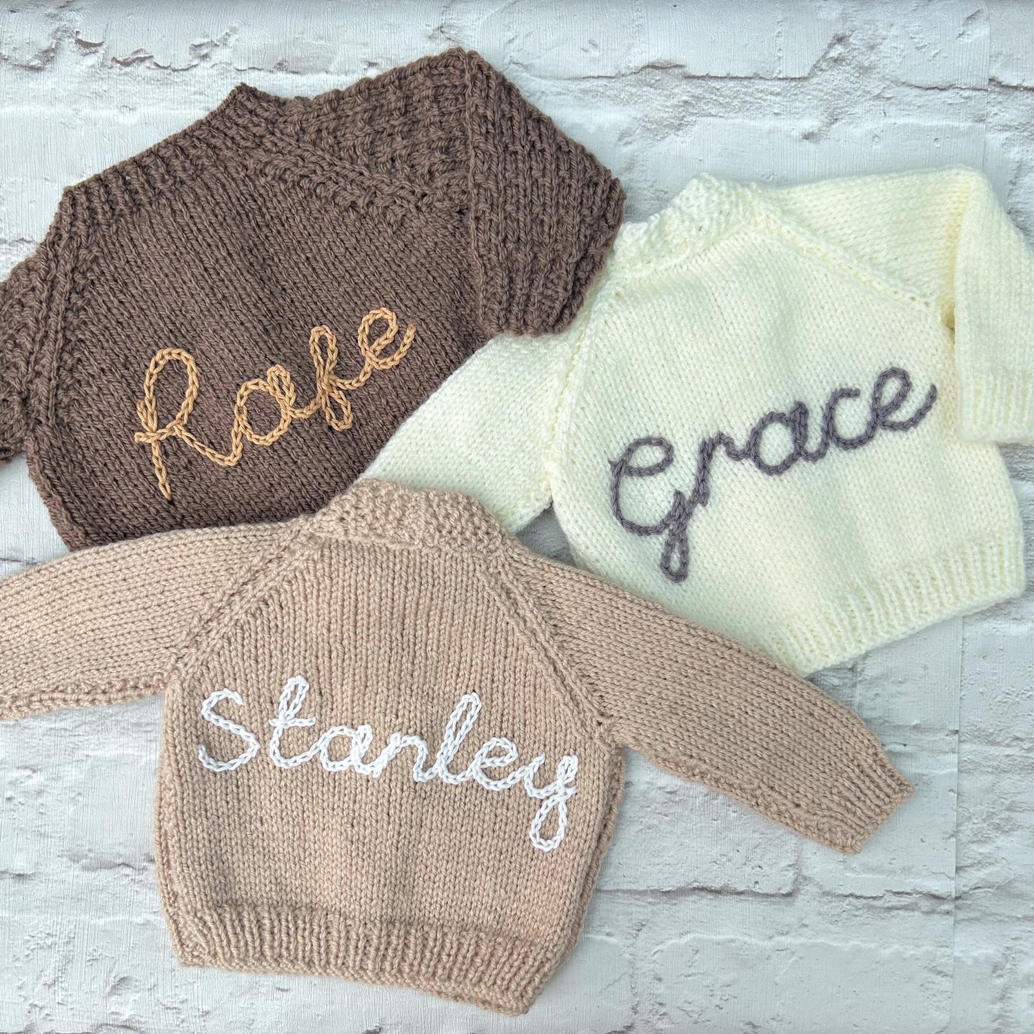 Selection of personalised hand knitted baby cardigans laid flat showing embroidered names in various colours | Little Name Knits

