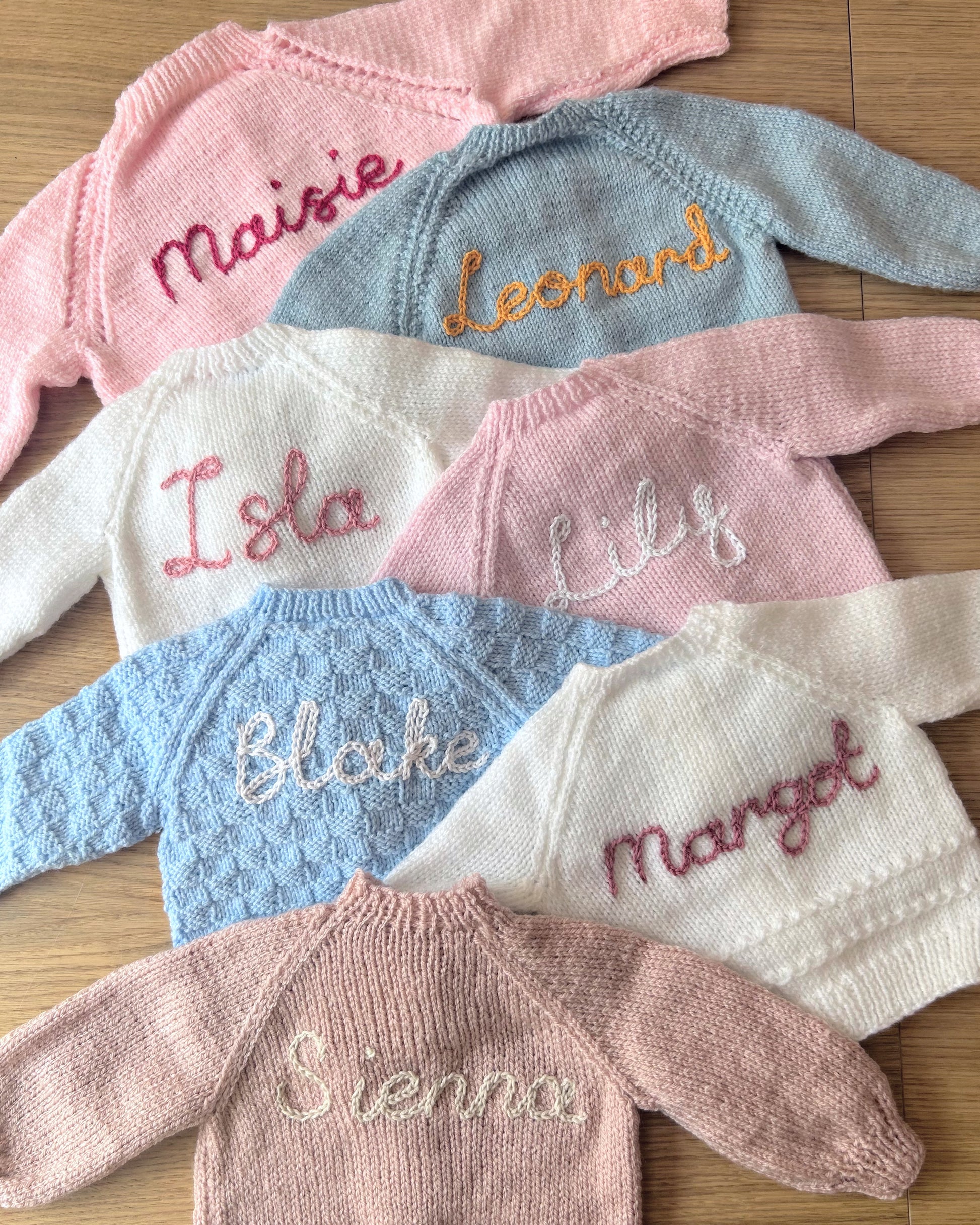Selection of personalised hand knitted baby cardigans laid flat showing embroidered names in various colours | Little Name Knits