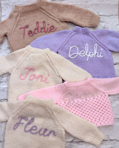 Selection of personalised hand knitted baby cardigans laid flat showing embroidered names in various colours | Little Name Knits

