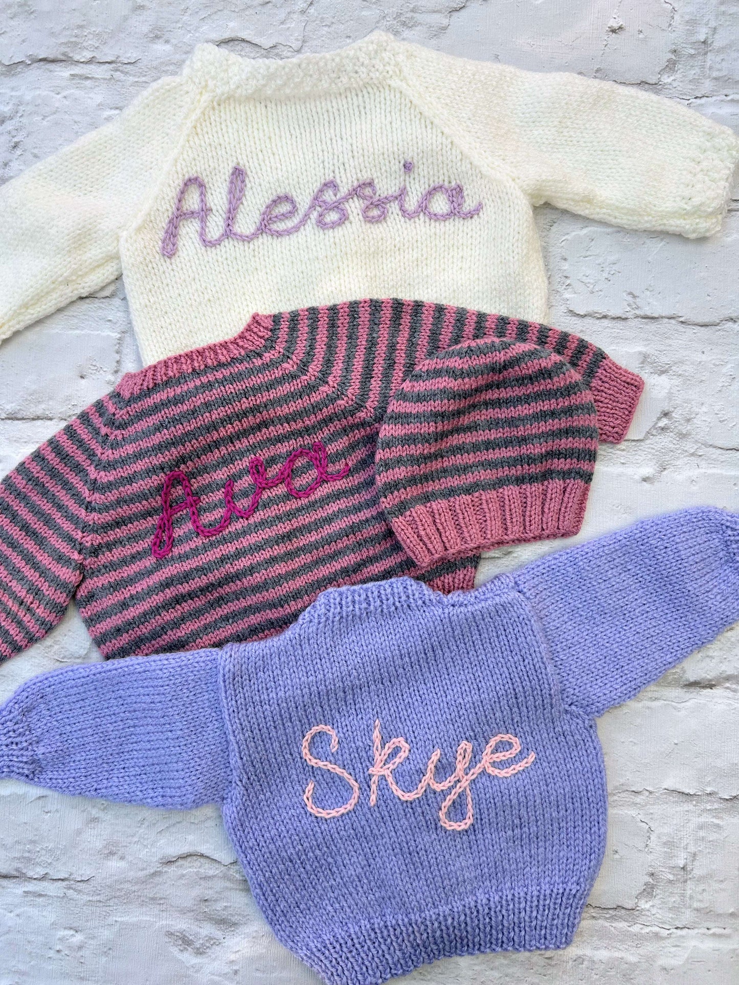 Selection of personalised hand knitted baby cardigans laid flat showing embroidered names in various colours | Little Name Knits

