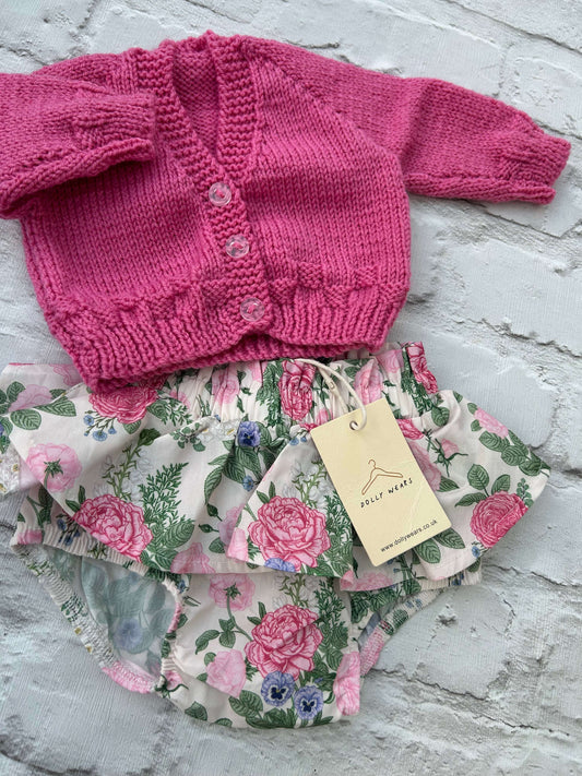 Pink knitted baby hand knitted cardigan to personalise with outfit of floral-patterned baby bloomers on a light gray surface.