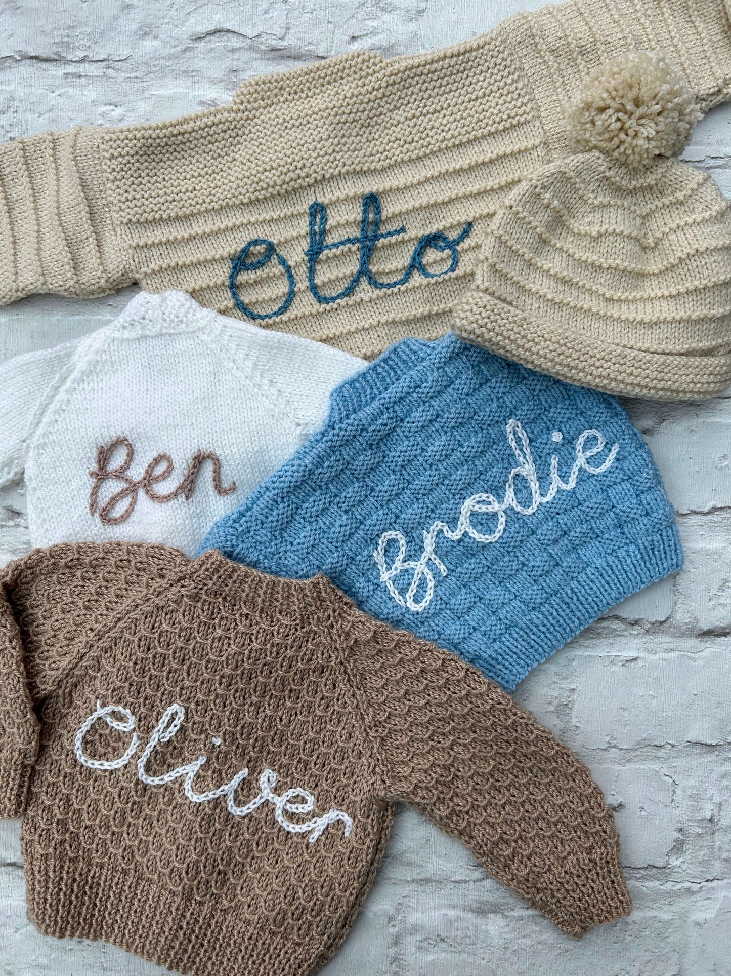 Selection of personalised hand knitted baby cardigans laid flat showing embroidered names in various colours | Little Name Knits