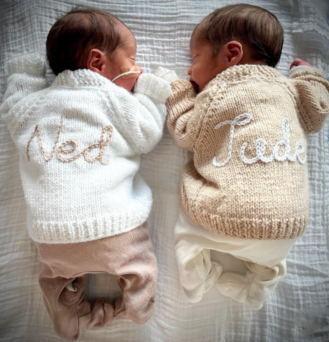 Example of previously made hand knitted cardigans featured on Baby twins Ned and Jude wearing white and beige hand knitted cardigans hand embroidered with their names 